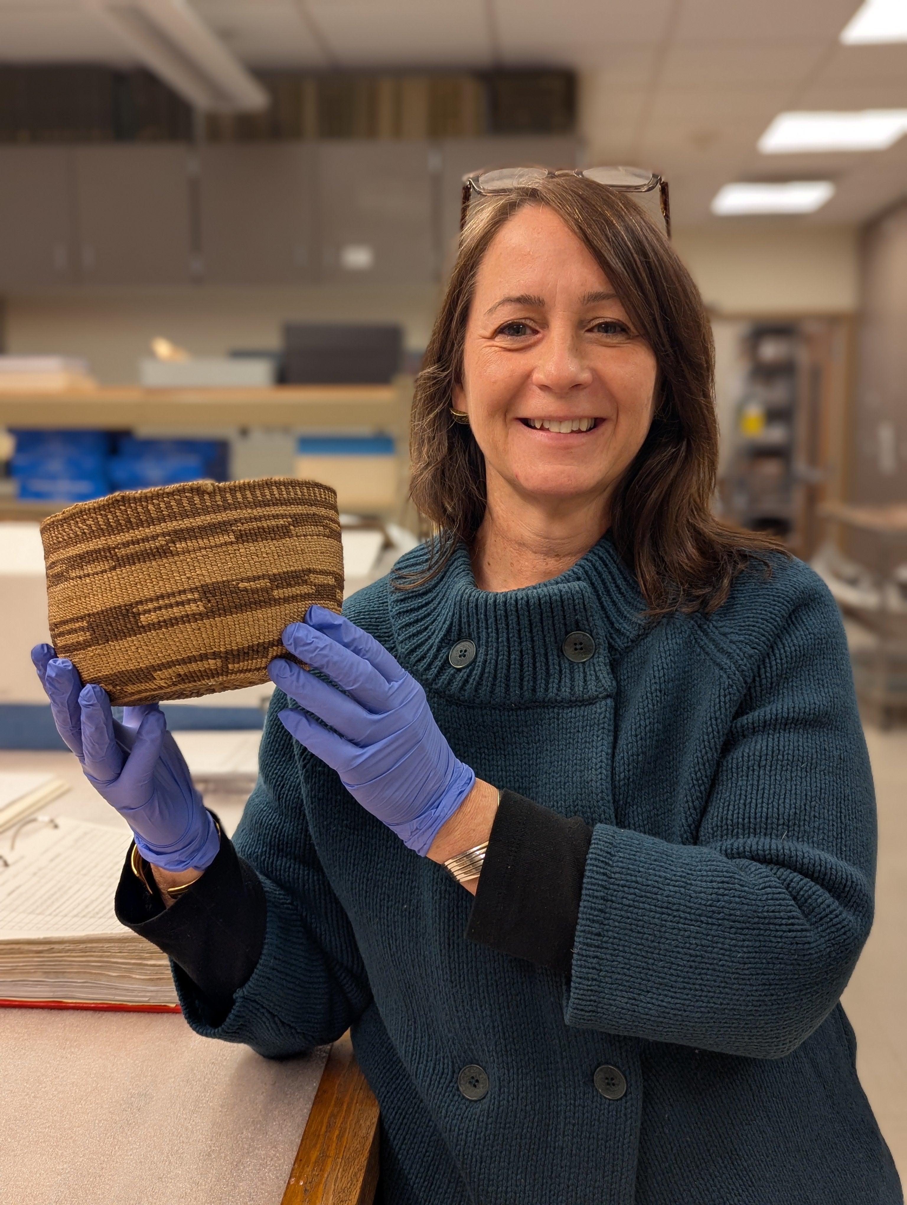 Elizabeth Kallenbach holds up a woven basket in museum Collections
