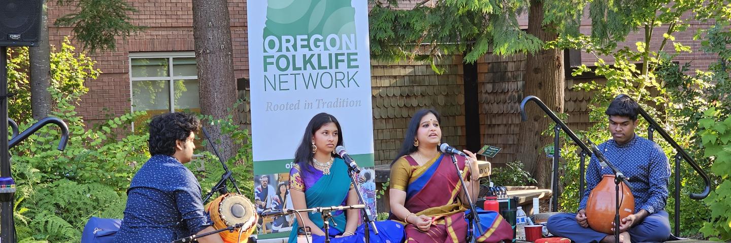 Two musicians and two singers perform Indian Carnatic Singing on a low stage outdoors.