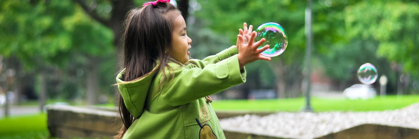 Little girl reaching for a bubble outside