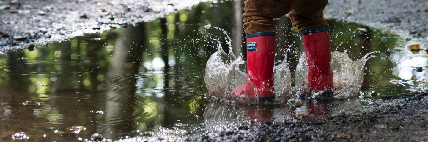 Preschooler jumping in a puddle with red boots