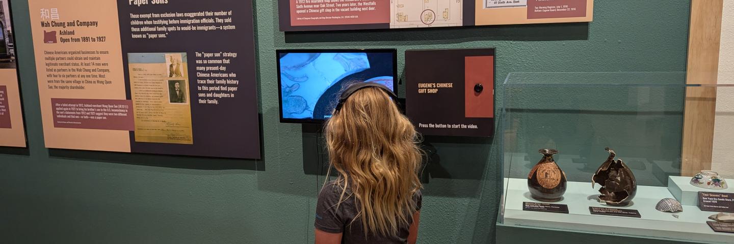 A child sits on a stool and watches a video in Roots and Resilience exhibit