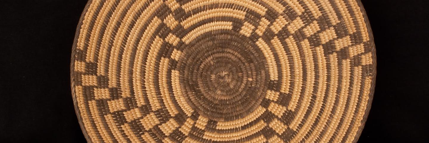 A top down image of a woven basket. Dark brown swirls are woven into the lighter tan basket. 