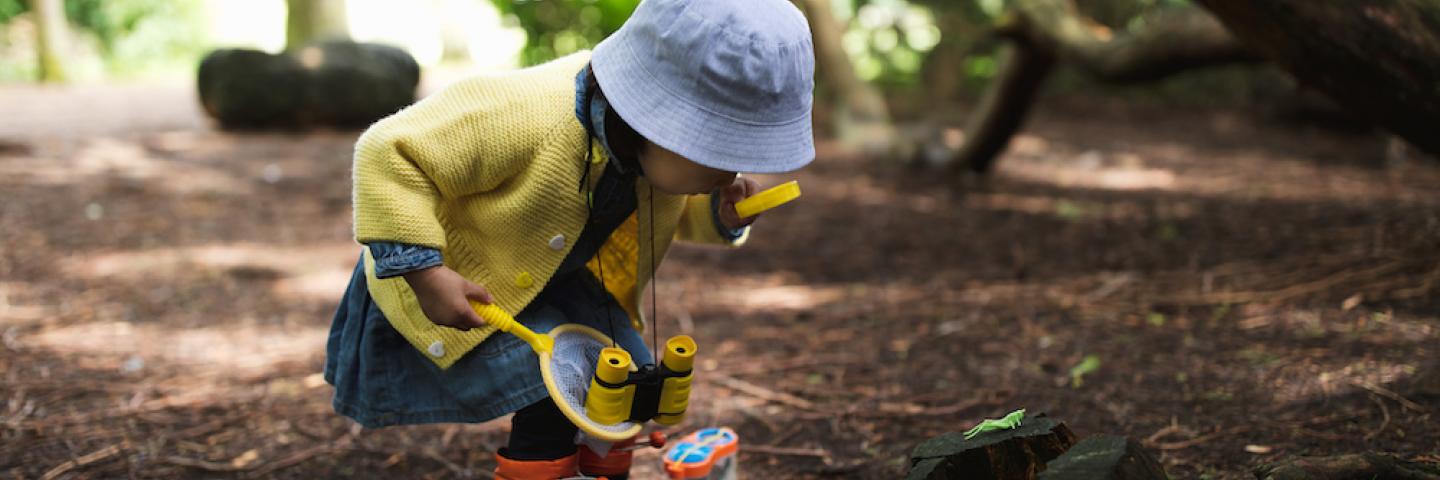 A child examining the forest floor using a yellow magnifying glass 