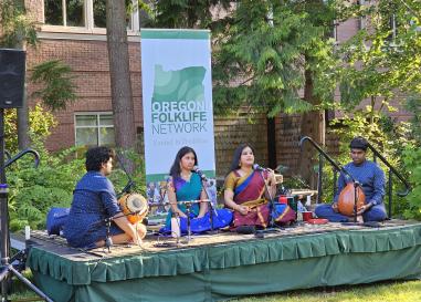 Two musicians and two singers perform Indian Carnatic Singing on a low stage outdoors.