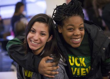 two students smiling at the camera, one with an arm around the other.
