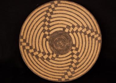 A top down image of a woven basket. Dark brown swirls are woven into the lighter tan basket. 