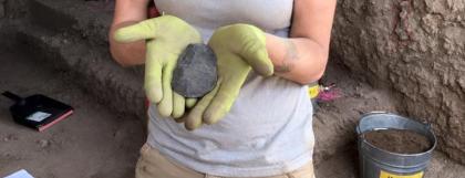 Woman with a hat and gloves on holding an artifact.