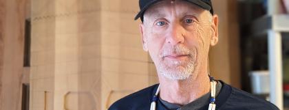 Greg Robinson stands in front of some of his wood carving and looks at the camera