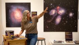 Education Manager Mia Jackson stands in front of two telescope images, presenting training information to museum volunteers.