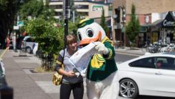The Oregon Duck holds a map and gives directions to a woman.