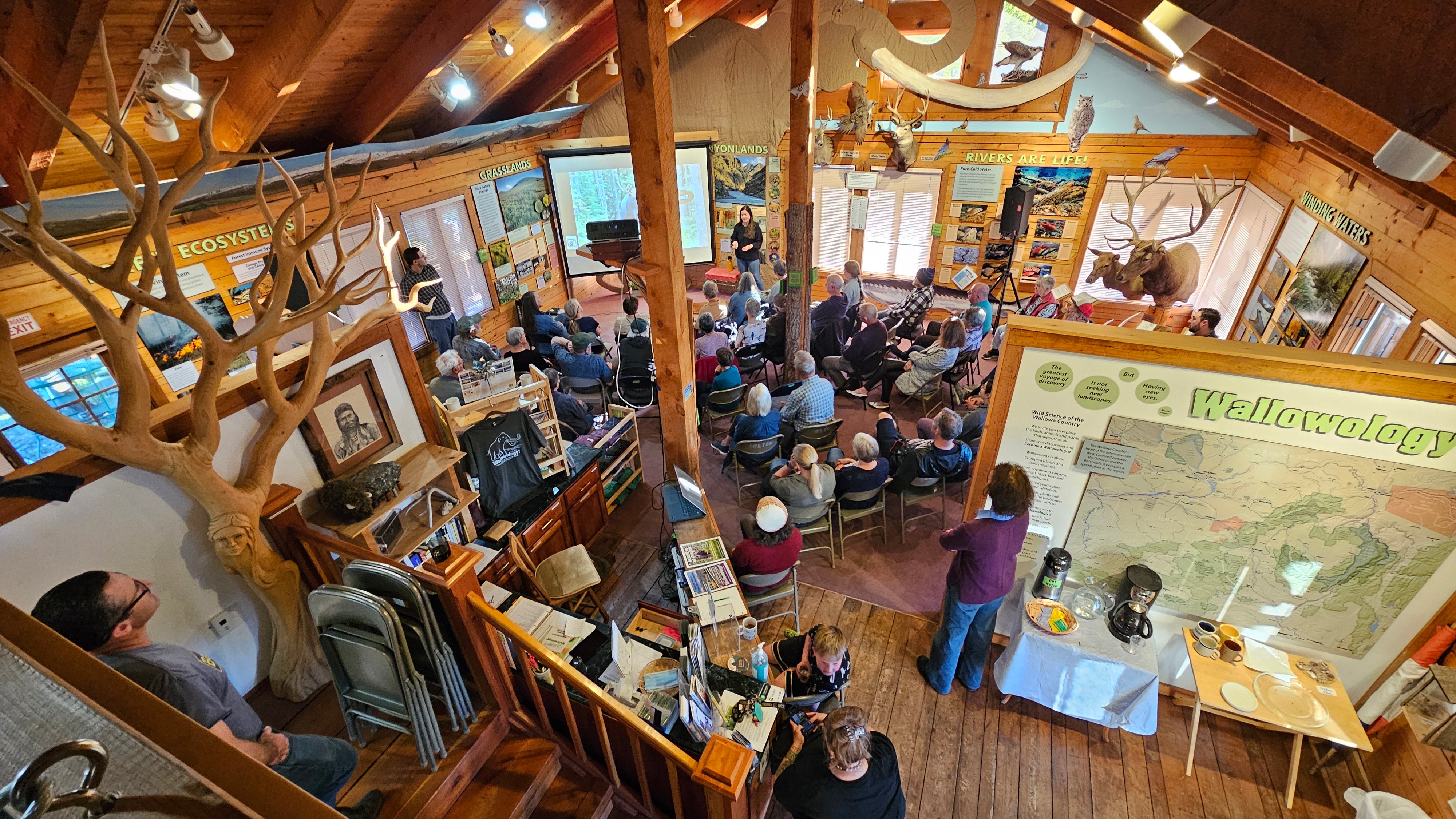An birds-eye view of a large exhibit hall in the style of an A-frame cabin. SA panel reading "Wallowology" is visible.